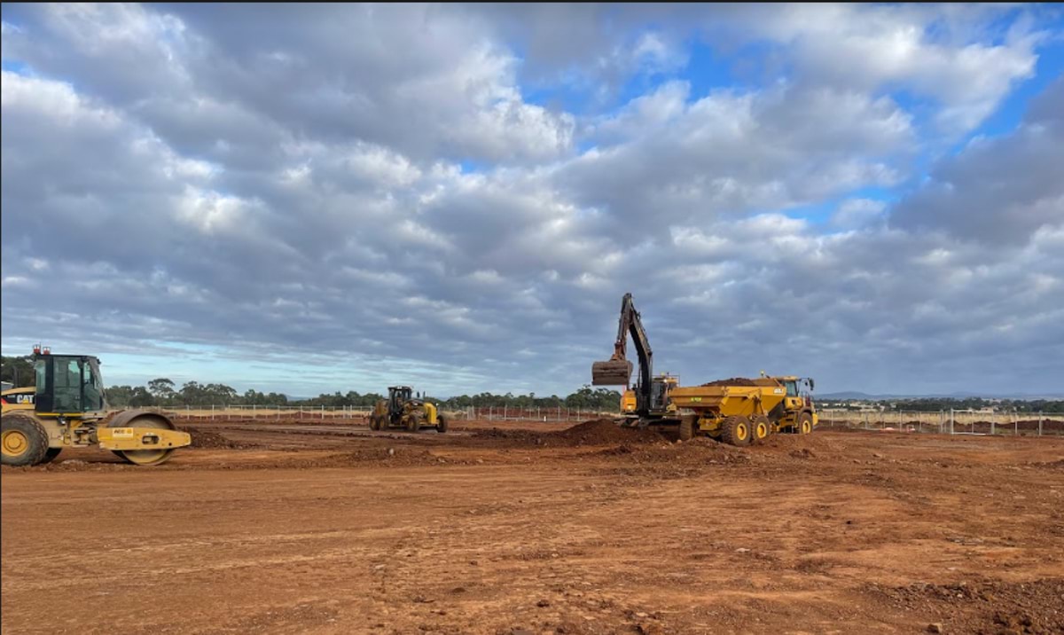 Aintree Specialist School (interim name) - construction photo of site progress in February 2023 - diggers and rollers on a red dirt paddock