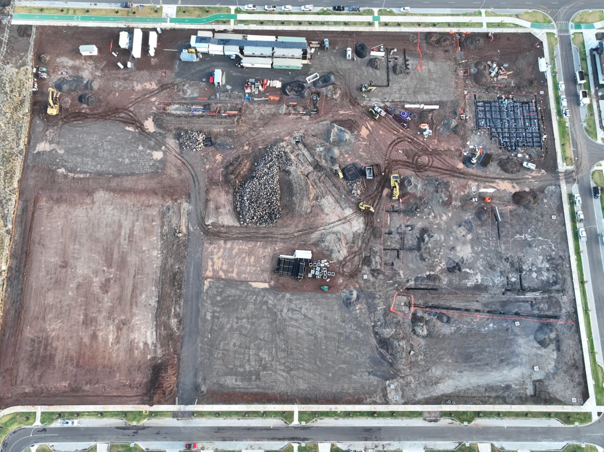 Tarneit North Primary School (interim name) - construction photo of site progress in February 2023 - aerial shot of site surrounded by access roads on 3 sides, flattened dark earth, construction vehicles and portables