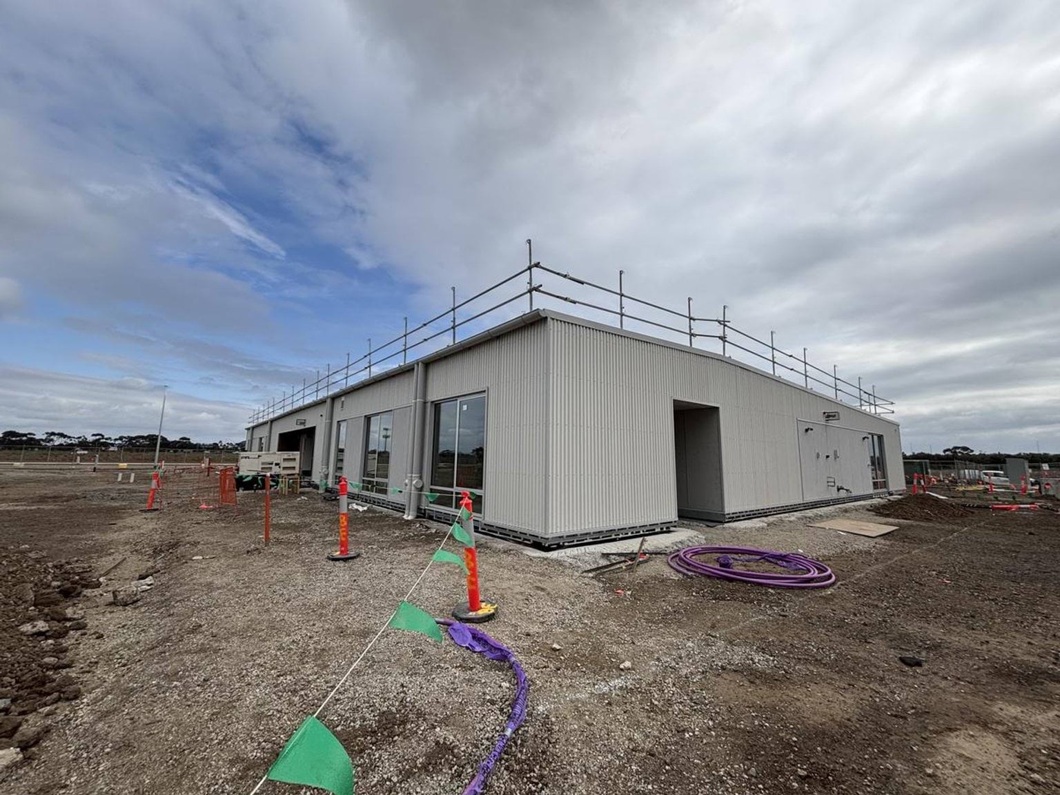 Constructed building with scaffolding along the guttering, surrounded by soil
