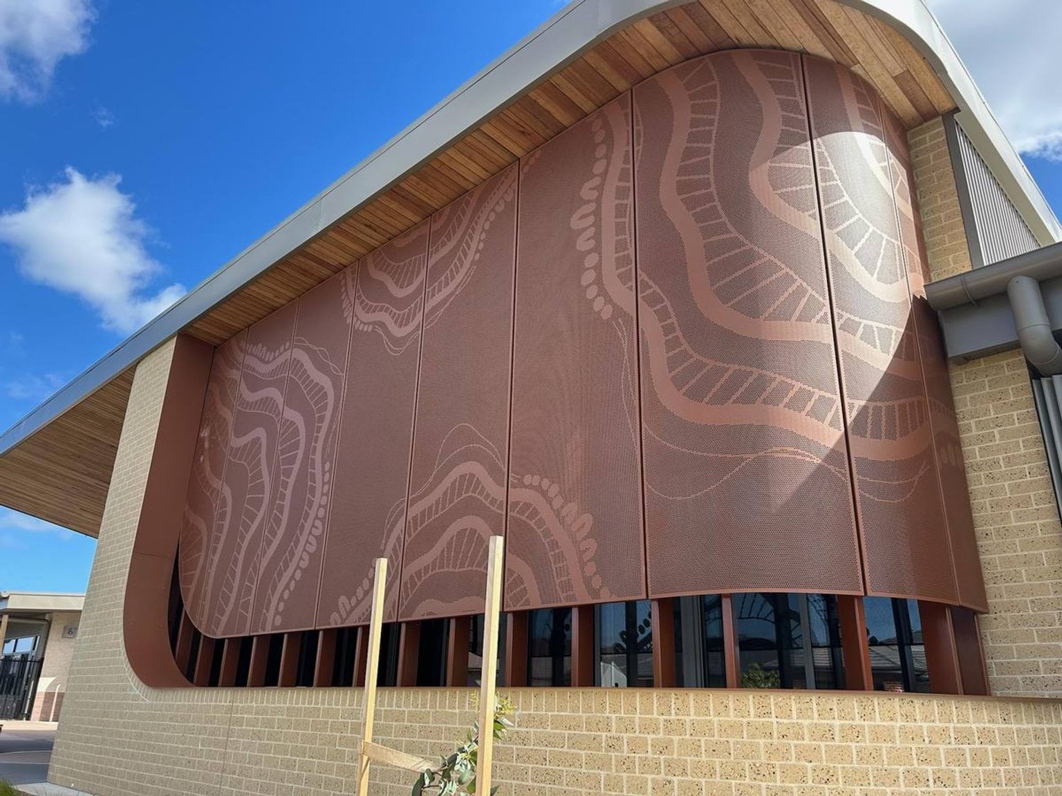 First Nations people design over external ochre coloured curved building. Brick work frames this feature. 