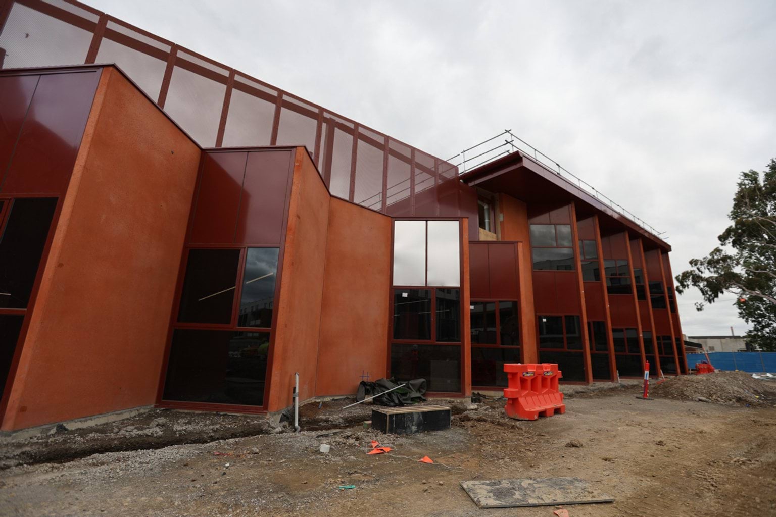 Side of school building with high roof and a modern design with corners down the side. There is construction equipment nearby.