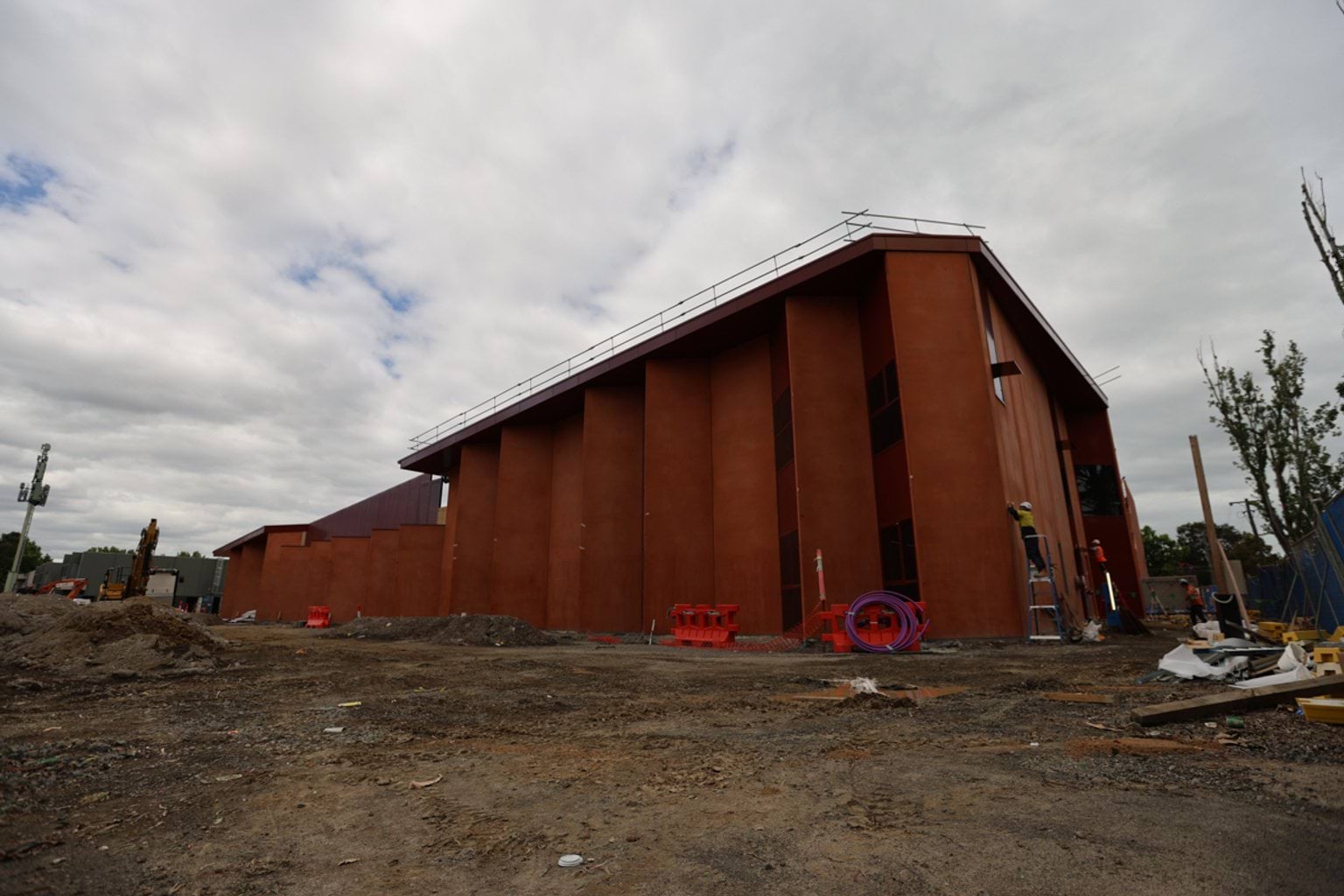 Multilevel school building under construction, as viewed from a low angle and zoomed out. It has orange walls and double doors with windows and scaffolding.
