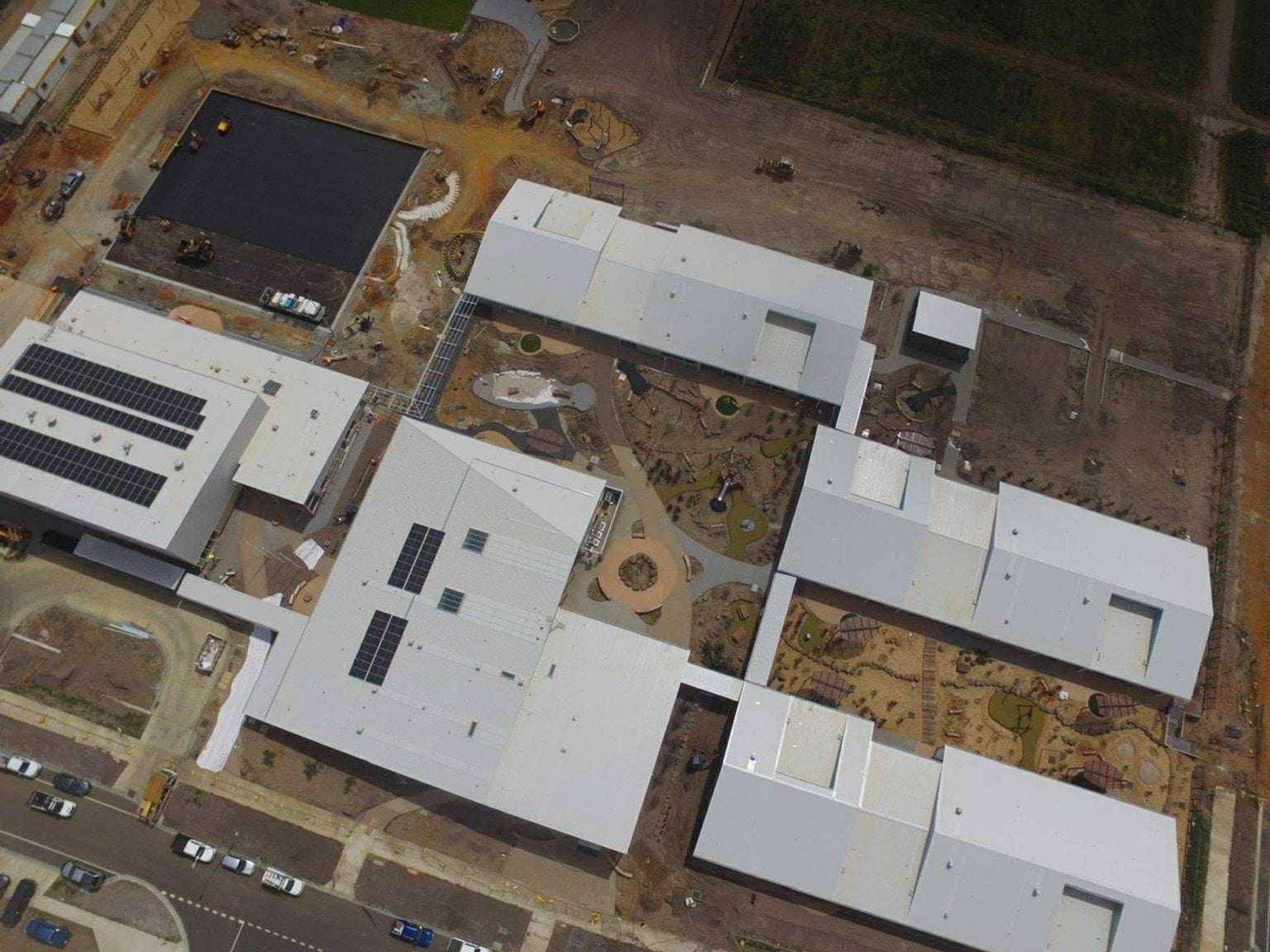 An aerial photo of the Balambalam Primary School construction progress in November. Lots of the buildings look mostly finished. Some have solar panels on the roof. The ground is mostly dirt with no trees or plants or grass.