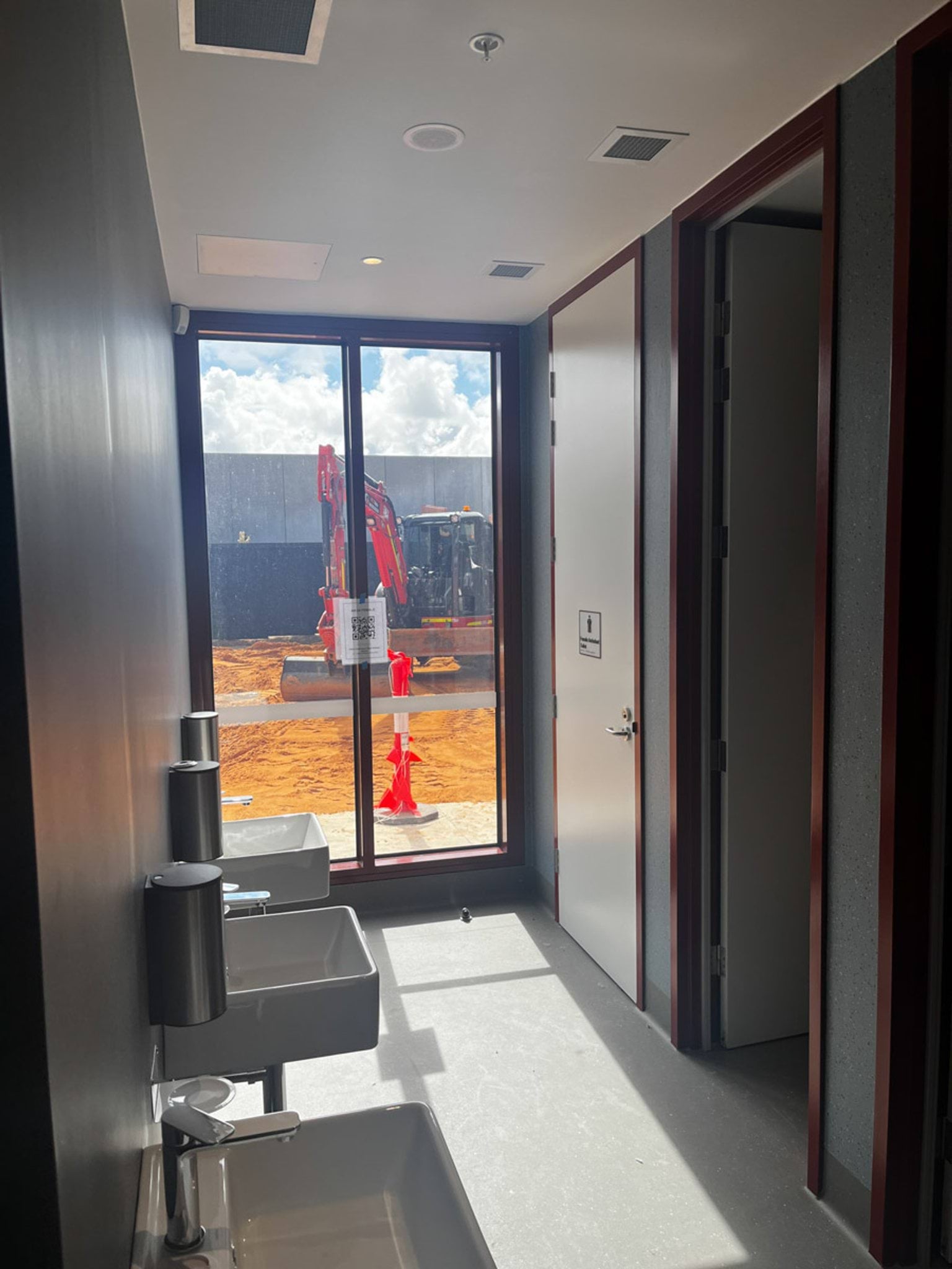 Glass door in bathroom area between sinks and toilet stalls