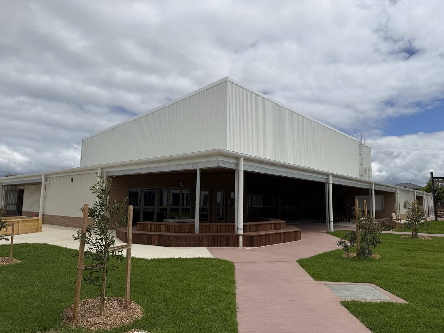 Outside Biyala Primary School, looking at a white building with wooden bench seating under a covered outside part. 