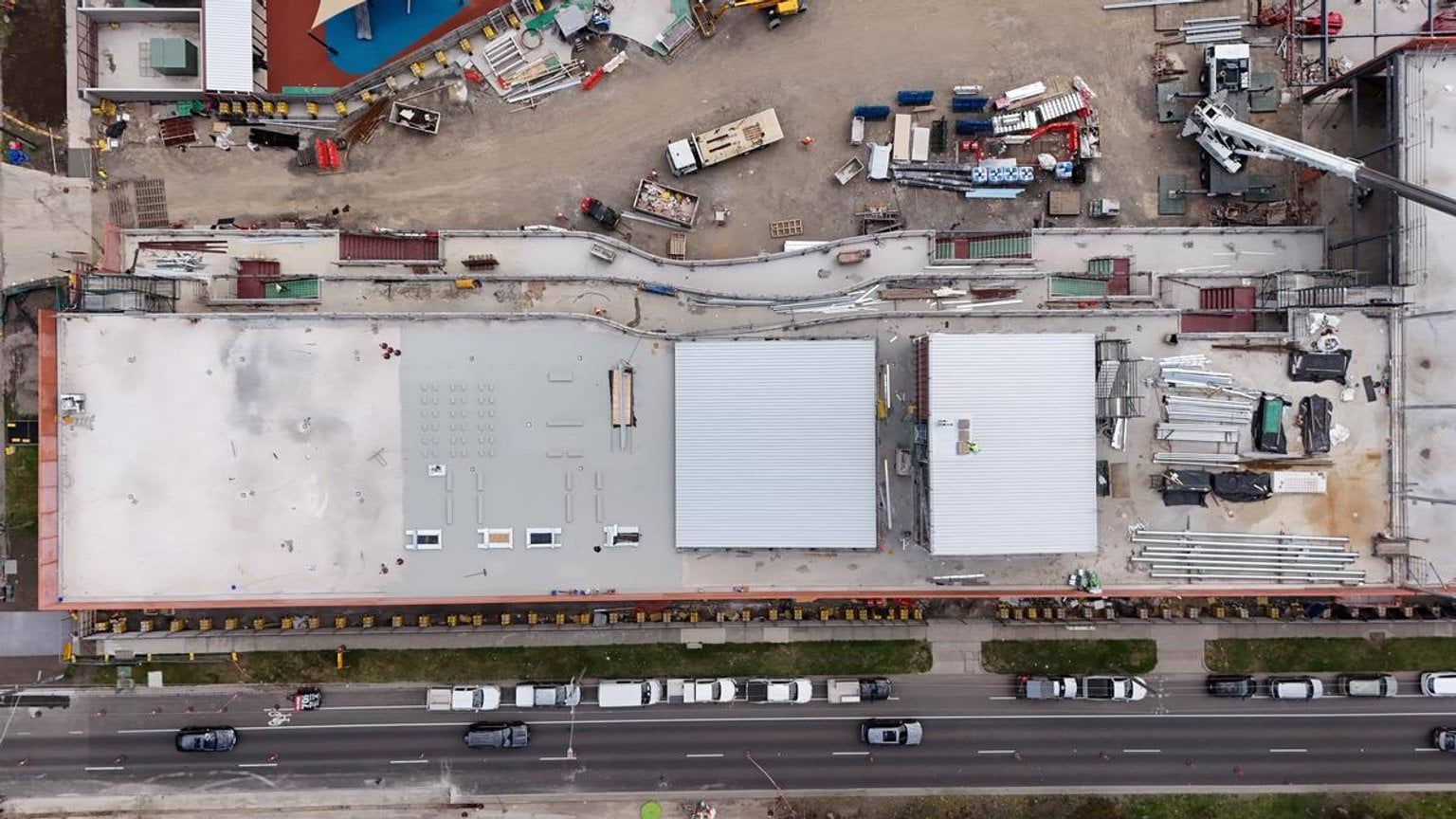 An overhead view of the school buildings with flat roofs, construction materials, and vehicles lined along the street.